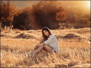 Zamyślona dziewczyna siedzi na uschniętej trawie