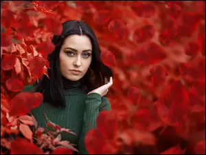 Dziewczyna o ciemnych włosach wygląda zza liści