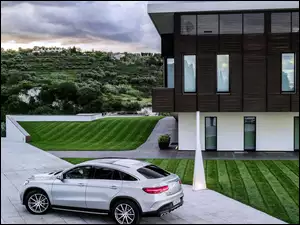 Biały samochód Mercedes GLE Coupe na podjeździe przed domem z widokiem na zielone wzgórze