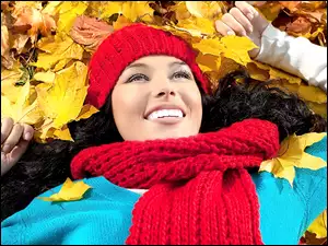 Kobieta w czapce i szaliku leżąca na liściach