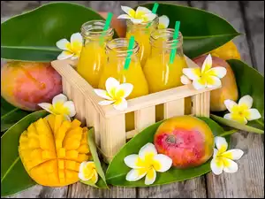 Butelki soku w skrzynce obok liści i mango