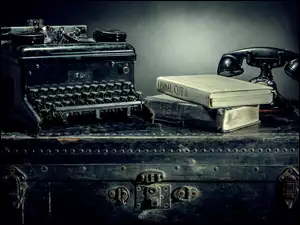 Maszyna do pisania książki oraz telefon położone na starej walizce