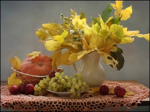 Dynia w koszyczku i kiście winogron obok wazonu z jesiennymi liśćmi