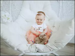 Uśmiechnięte dziecko z kotem na fotelu