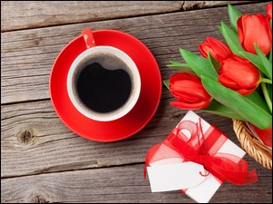 Filiżanka kawy obok prezentu i czerwonych tulipanów