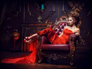 Kobieta w fryzurze i makijażu w czerwonej sukni na fotelu