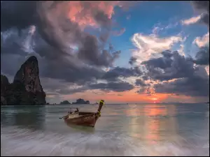 Zachód słońca nad skalną morską plaża z łódką w Tajlandii