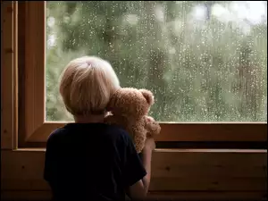 Chłopiec z misiem w deszczowym oknie