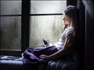Smutna dziewczyna w oknie z kotem w czasie deszczu