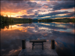 Pomost z ławeczką nad jeziorem oświetlonym zachodem słońca