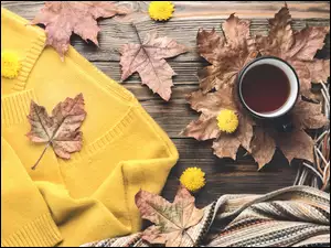 Kubek kawy z swetrem szalem i jesiennymi liśćmi