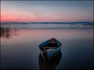 Łódka na zamglonym jeziorze o zachodzie słońca