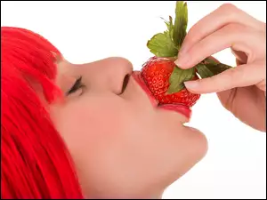 Dziewczyna z czerwonymi włosami je truskawkę