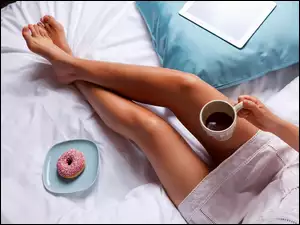 Kubek z kawą w dłoni kobiety siedzącej na łóżku