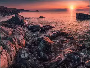 Skały na brzegu morza w blasku czerwono zachodzącego słońca