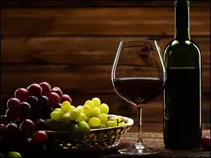 Kiście winogron w koszyczku obok butelki i kieliszka z winem