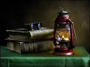 Lampa naftowa postawiona na stole obok książek