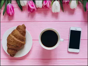 Rogalik kawa i telefon obok tulipanów