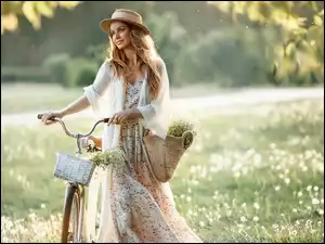 Kobieta w kapeluszu z rowerem na łące