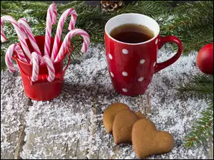 Kubek herbaty obok ciasteczek i lizaków w wiaderku na sztucznym śniegu