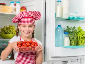 Dziewczyna z kapeluszem kucharza i pudełkiem pomidorów przed lodówką