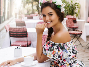 Uśmiechnięta kobieta w wianku obok filiżanki kawy
