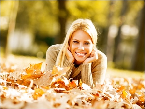 Uśmiechnięta obieta leżąca na jesiennych liściach