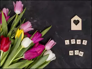 Drewniany domek i napis Love Mom obok kolorowych tulipanów