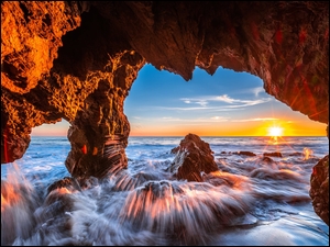Widok z rozświetlonej jaskini na zachód słońca nad morzem