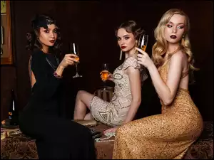 Trzy kobiety w wieczorowych sukniach z kieliszkami w rękach
