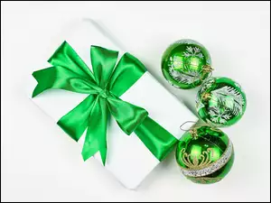 Zielone bombki obok prezentu z zieloną kokardą na białym tle