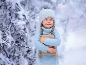 Dziewczynka w wełnianej czapce z prezentem przy ośnieżonych krzewach