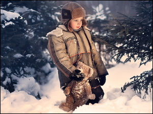Chłopiec z pluszowym misiem w zimowym lesie
