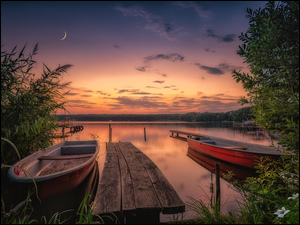 Drewniany pomost i łodzie na brzegu jeziora o zachodzie słońca