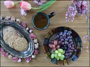 Talerze z winogronami i ciasteczkami do filiżanki kawy i tulipanów