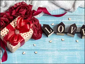 Napis Love z klocków obok prezentu i sztucznych róż