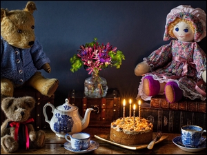Lalka i misie pluszowe obok ciasta, bukietu kwiatów i zastawy kawowej
