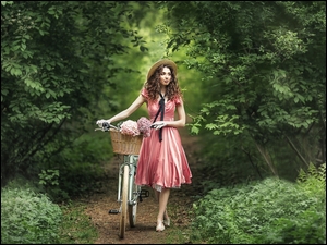 Kobieta w kapeluszu z rowerem na leśnej ścieżce