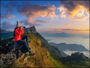 Kobieta na skałach fotografująca zamglone góry
