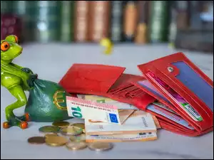 Figurka żaby z workiem obok portfeli monet i banknotów