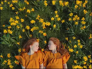 Dwie dziewczynki z rudymi włosami leżącemiędzy kwiatami na trawie