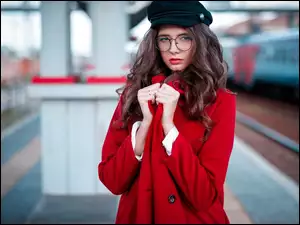 Kobieta w czerwonym płaszczu stoi na peronie
