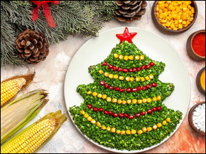 Kolby kukurydzy i zielone gałązki obok talerza z warzywami ułożonymi w kształcie choinki