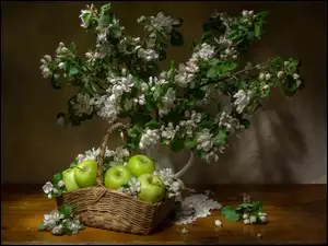 Kwitnące gałązki w dzbanku obok koszyczka z jabłkami