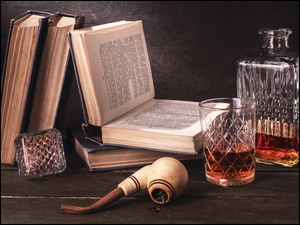 Fajka obok książek i alkoholu w szklance i karafce