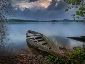 Łódka na brzegu jeziora pod zachmurzonym niebem