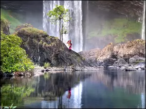 Na skale przy wodospadzie stoi dziewczyna