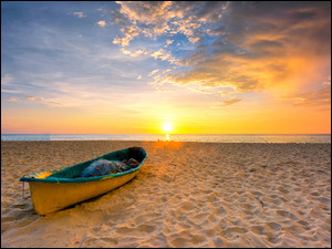 Stara łódka nad plaży w blasku zachodzącego słońca