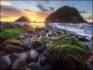 Omszałe kamienie nad brzegiem morza w blasku zachodzącego słońca