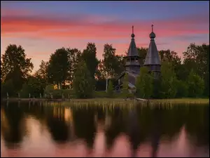 Cerkiew wśród drzew nad jeziorem pod zaróżowionym niebem
